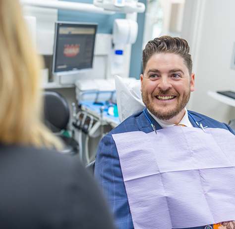 Man in dental chair smiling at female dental team member