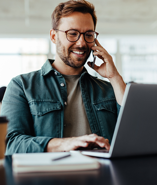 Man talking on phone and typing on laptop