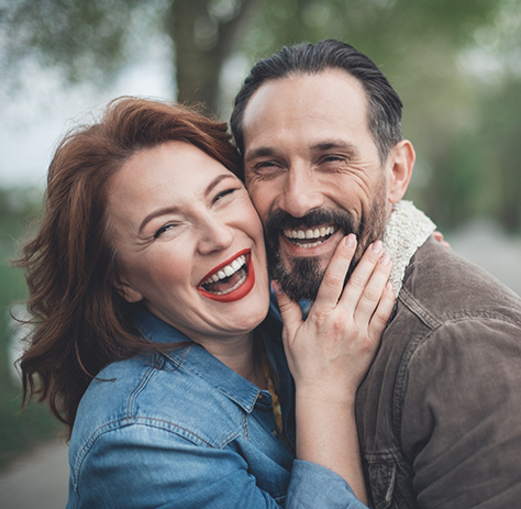 Smiling woman hugging smiling man from side