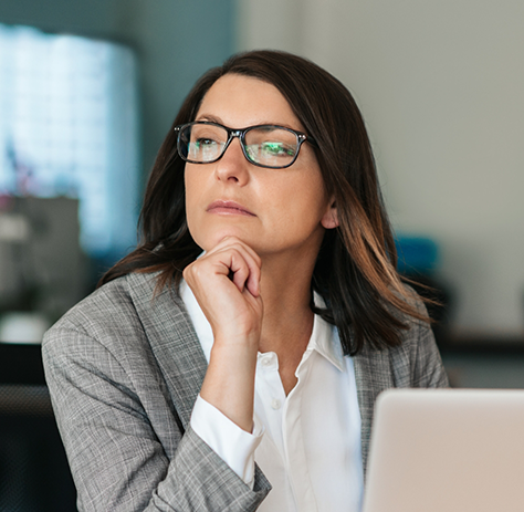 Woman with glasses sitting at computer looking thoughtful