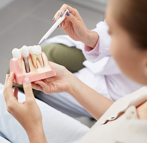 Dental patient holding and looking at model of dental implant