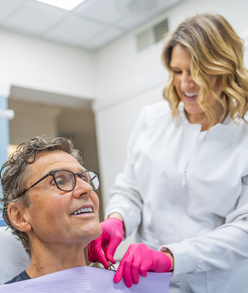 Female dentist adjusting cloth for male dental patient