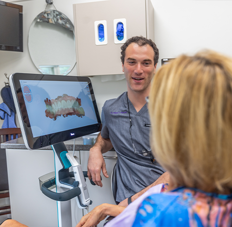 Standing next to scan of teeth on monitor and talking to dental team member