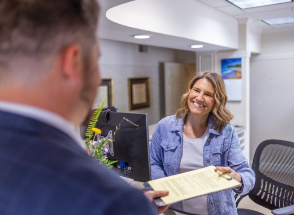 Woman handing form on clipboard to man in suit