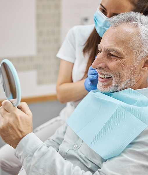 Man in dental chair checking smile in mirror