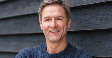 Older man standing in front of wooden wall smiling