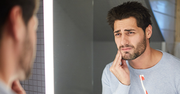 Man looking in bathroom mirror rubbing jaw in pain