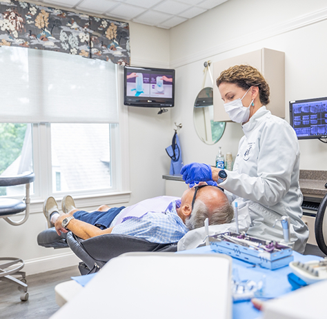 Older male patient having teeth cleaned by female dentist with mask