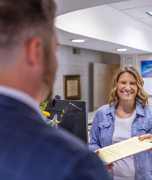 Female patient handing form on clipboard to man at front desk